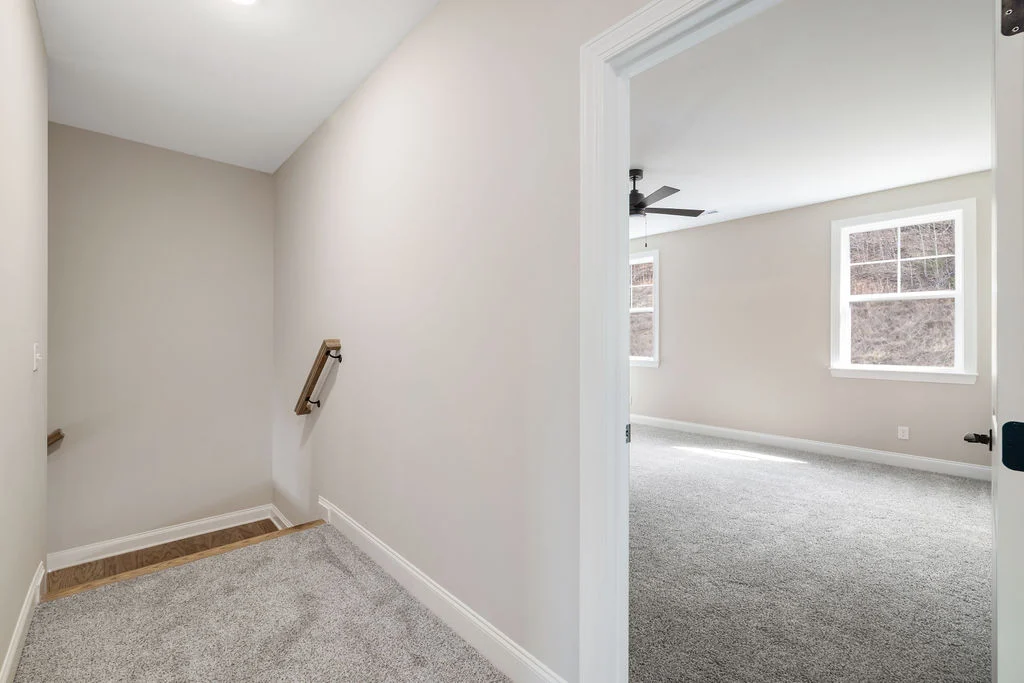 Carpeted hallway leading to a bright room with two windows and a ceiling fan, by Pratt Home Builders in Chattanooga TN.