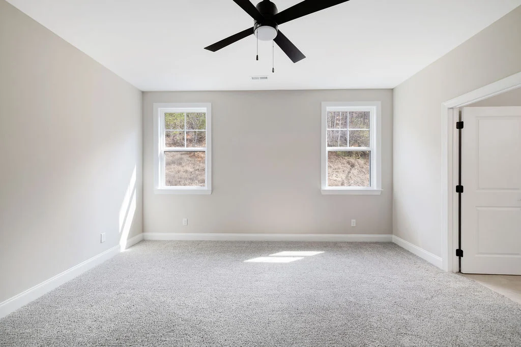 Bright, spacious room with light grey walls, carpet, and two windows. Ceiling fan centered above. Built by Pratt Home Builders in Chattanooga TN.