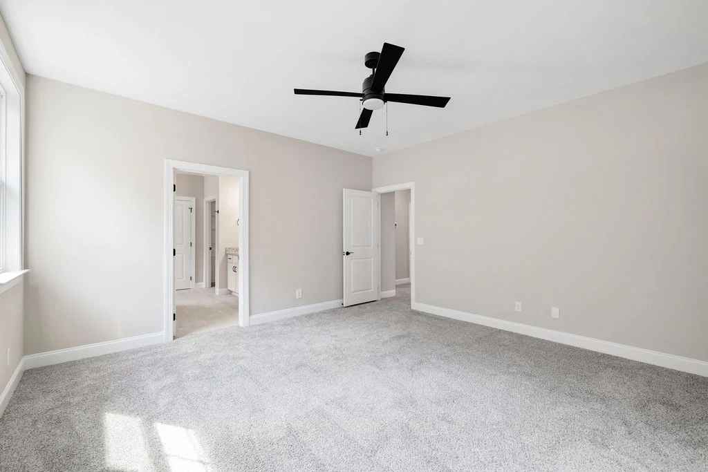 Spacious bedroom with carpet, neutral walls, ceiling fan, and two doorways leading to adjoining rooms. Built by Pratt Home Builders in Chattanooga TN.