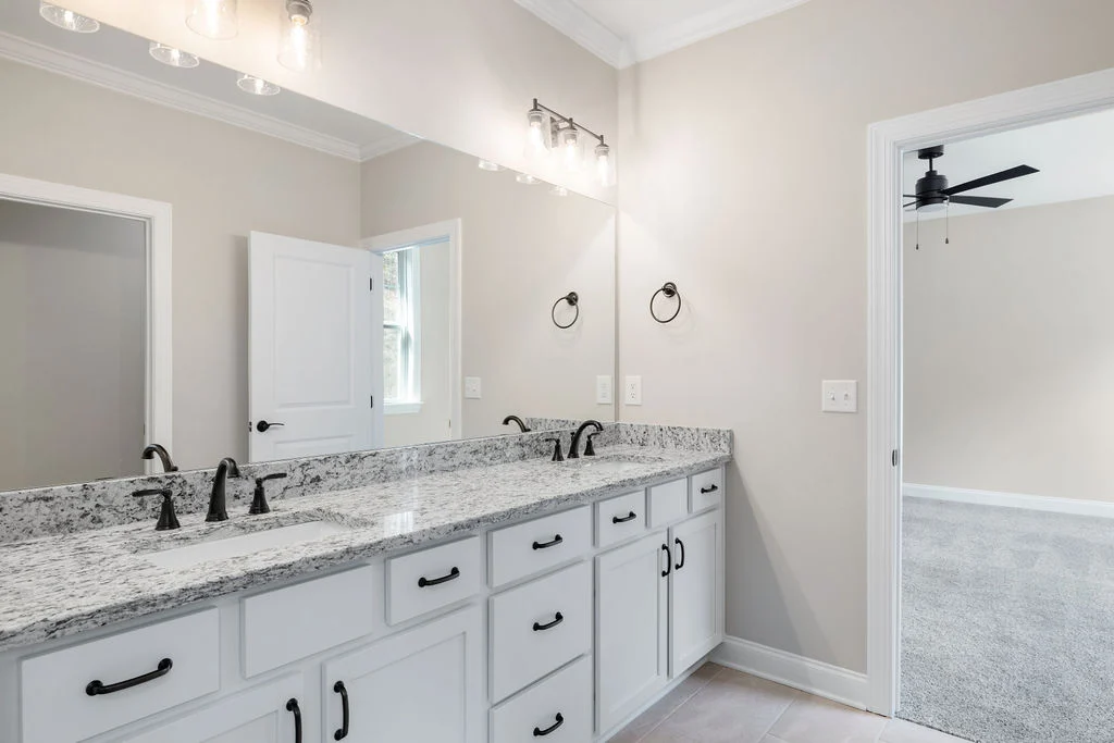 Modern bathroom with dual sinks, granite countertop, and chrome fixtures; adjacent to carpeted room, crafted by Pratt Home Builders in Chattanooga TN.