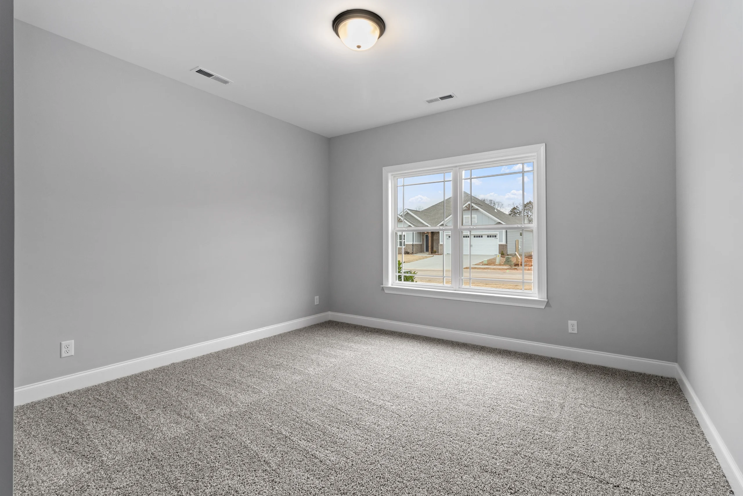 Empty gray-walled room with carpet flooring, large window overlooking a suburban street. New construction by Pratt Home Builders in Chattanooga TN.