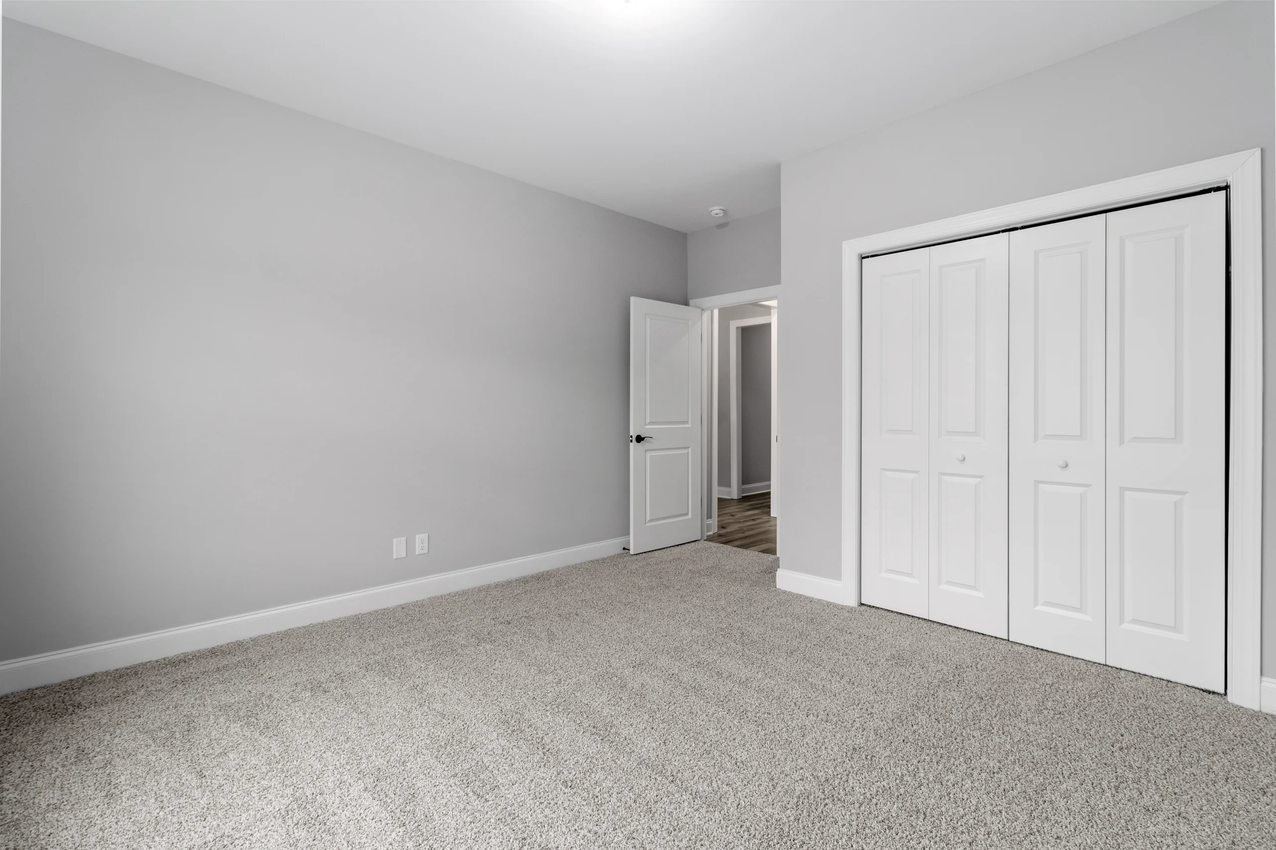 Empty room with gray walls, beige carpet, and white closet doors. Open door reveals wood flooring. Pratt Home Builders in Chattanooga TN.