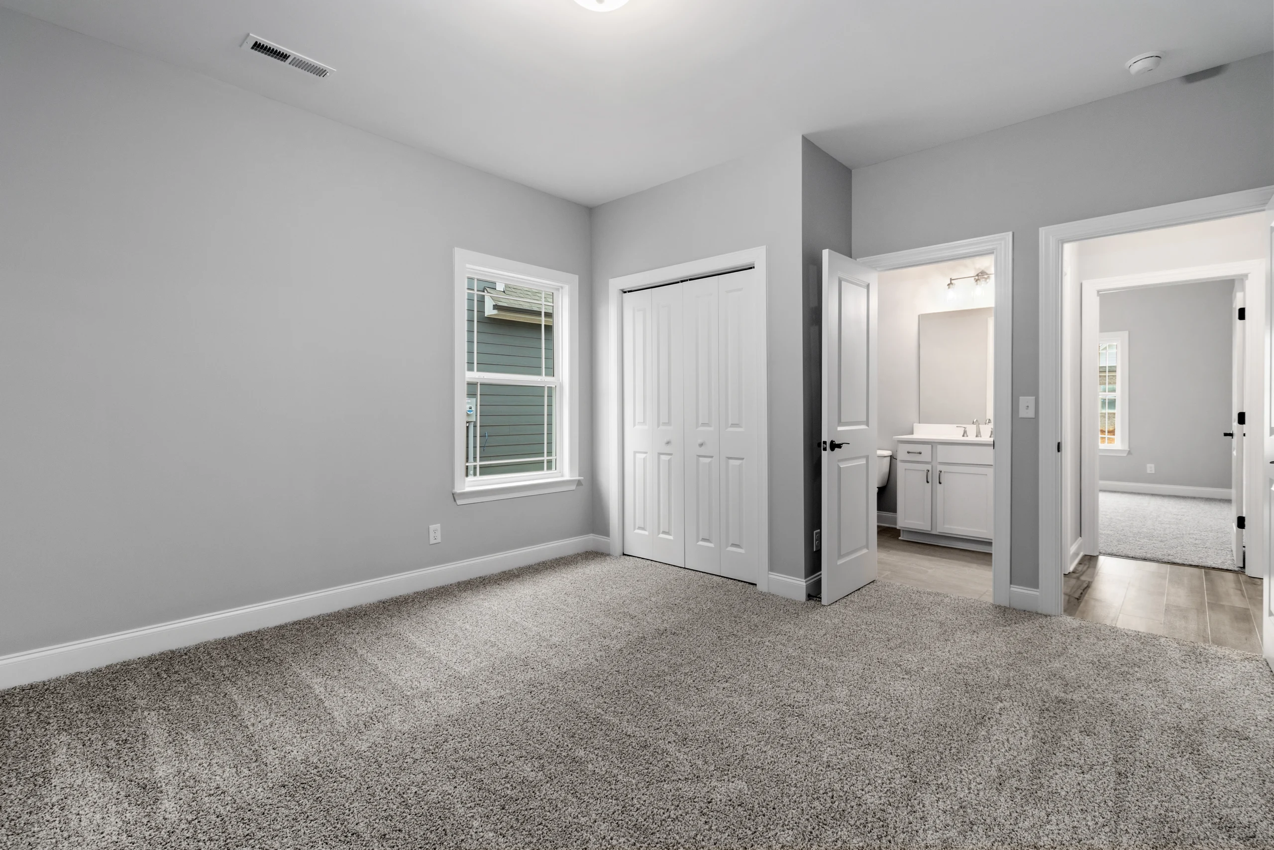 Empty gray-carpeted room with white walls, window, closet, and bathroom, designed by Pratt Home Builders in Chattanooga TN.