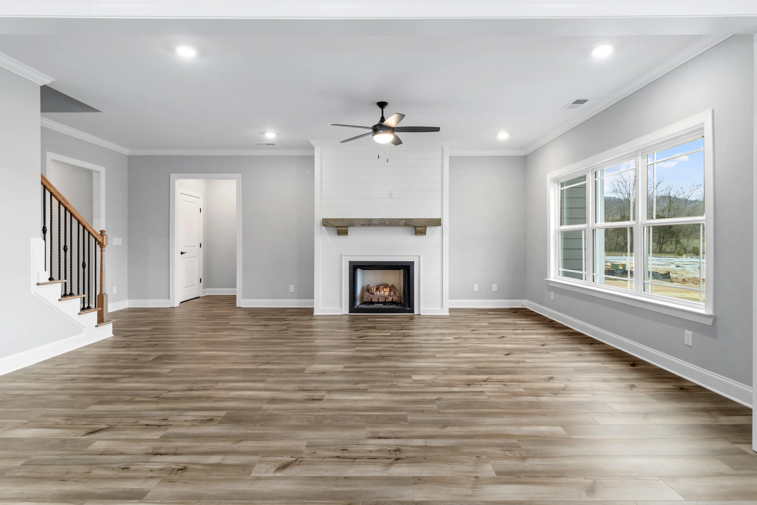 Spacious living room with hardwood floors, white fireplace, and large windows. Pratt Home Builders in Chattanooga TN.