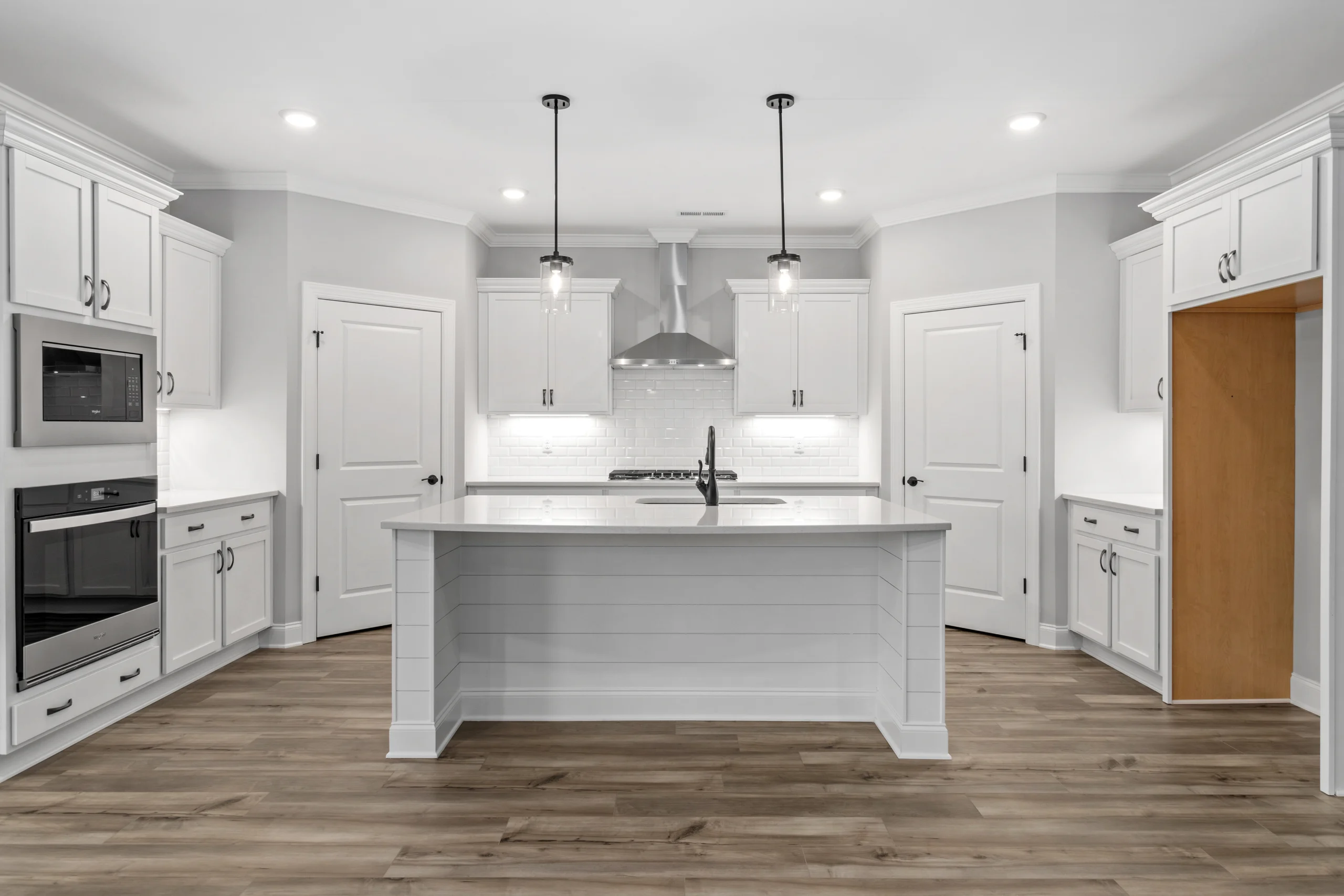Modern kitchen with white cabinets, island, and stainless steel appliances by Pratt Home Builders in Chattanooga TN. Wood flooring and pendant lights.