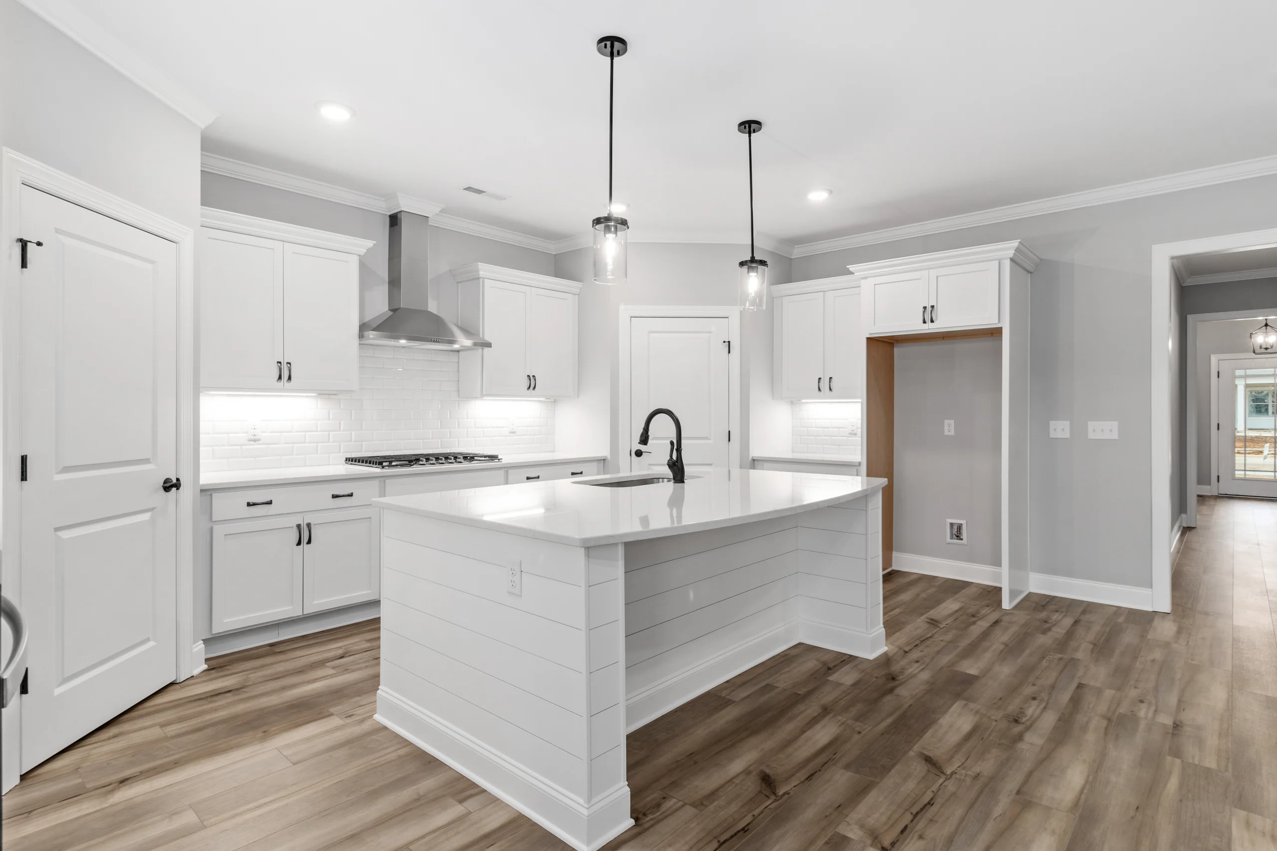 Modern kitchen by Pratt Home Builders in Chattanooga TN with white cabinets, island, pendant lights, and wood floors.