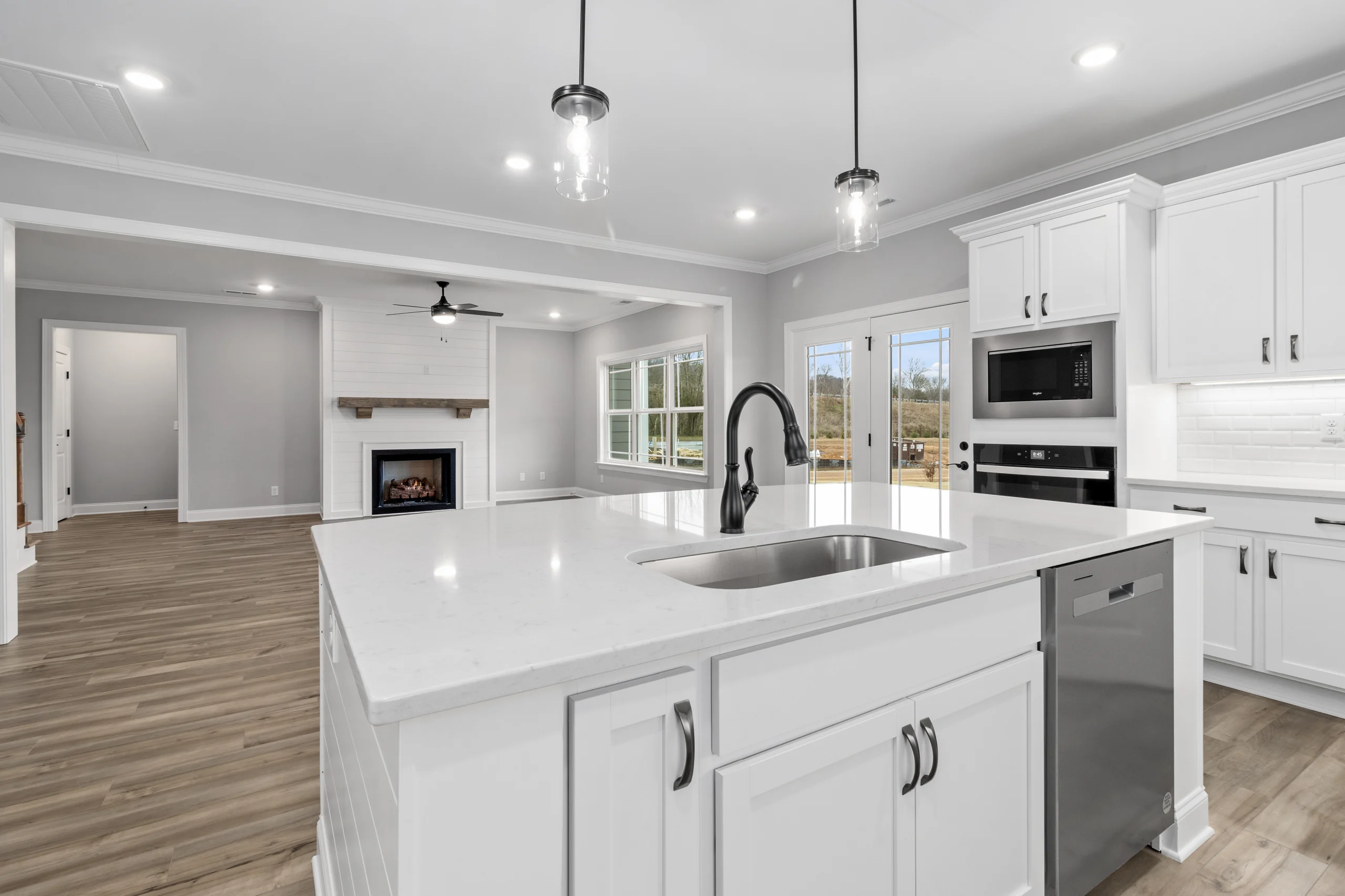 Modern kitchen and living area by Pratt Home Builders in Chattanooga TN; white cabinets, island with sink, fireplace, hardwood floors, ample lighting.