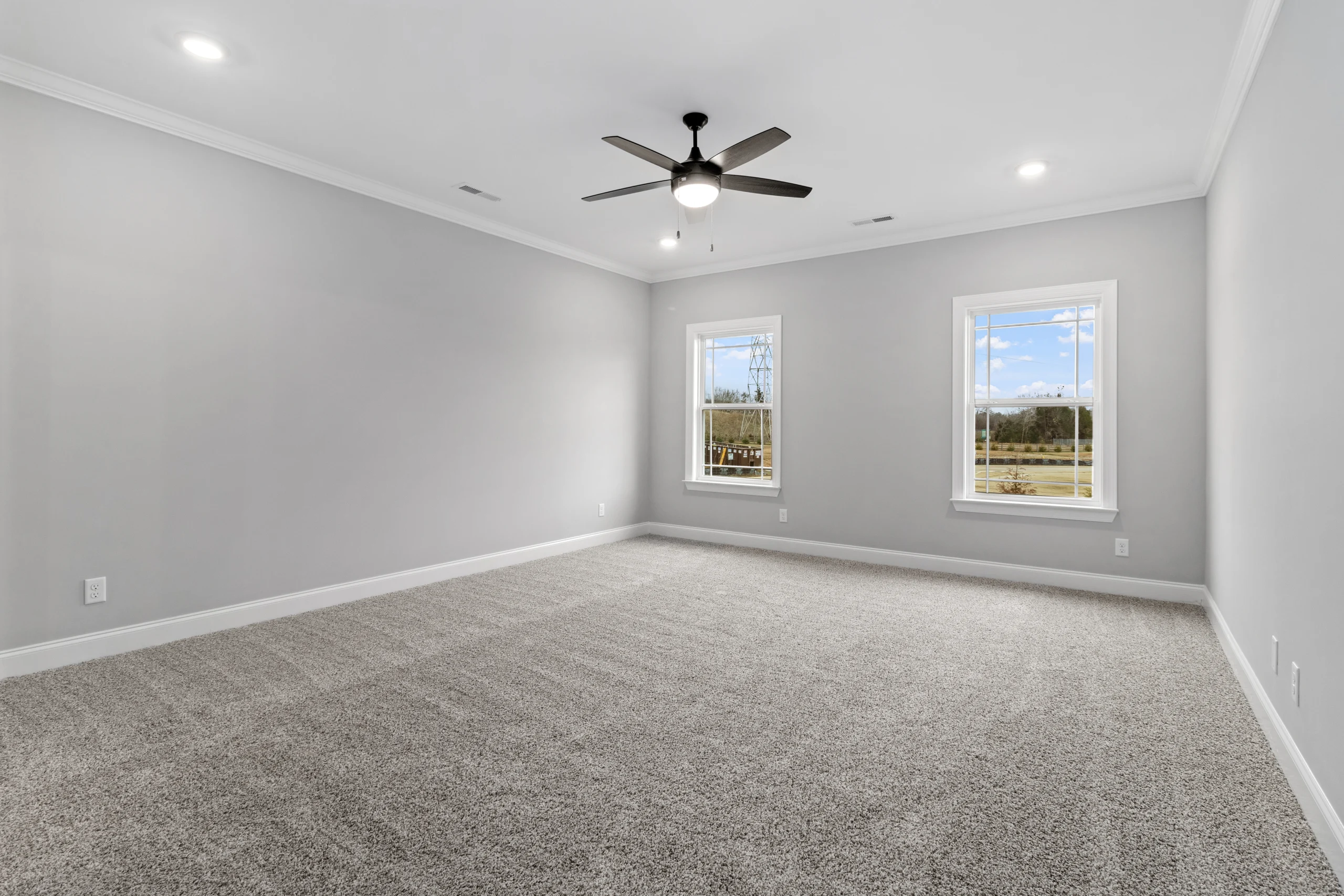 Spacious gray carpeted room with ceiling fan and two sunlit windows, designed by Pratt Home Builders in Chattanooga TN.