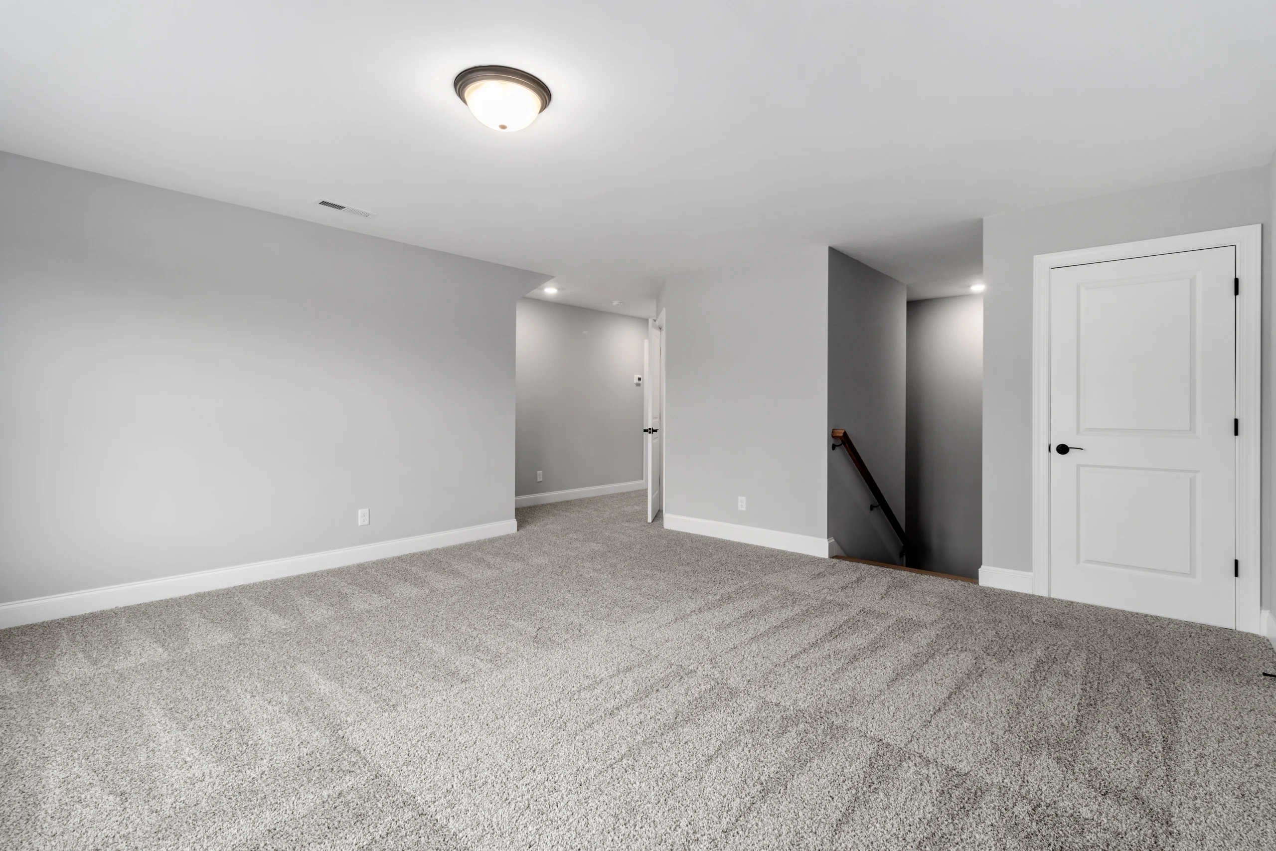 Spacious gray-carpeted room with white walls, ceiling light, and stairway by Pratt Home Builders in Chattanooga TN.