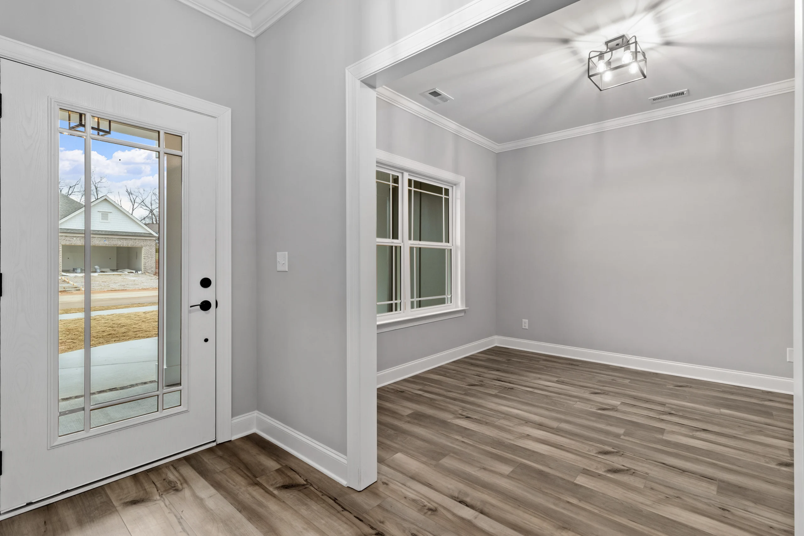 Entryway with glass door, adjacent room, hardwood floors, and modern light fixture by Pratt Home Builders in Chattanooga TN.