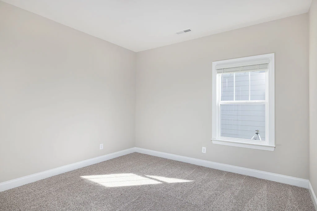 Empty room with beige walls and carpet, natural light from a single window. Interior by Pratt Home Builders in Chattanooga TN.