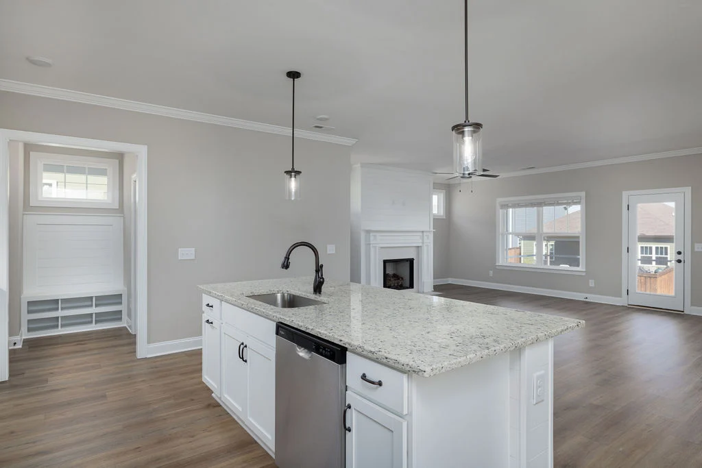 Bright, open-concept kitchen and living room with white cabinets, granite island, fireplace, and hardwood floors by Pratt Home Builders in Chattanooga