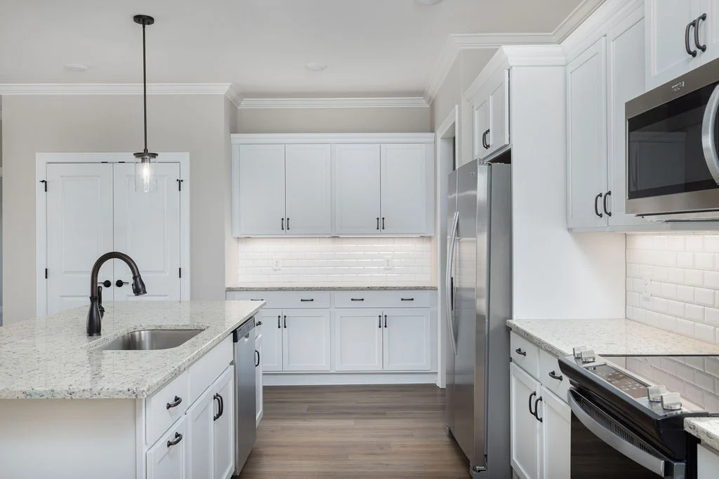 Modern kitchen with white cabinets, gray granite countertops, stainless steel appliances, and pendant lighting by Pratt Home Builders in Chattanooga T