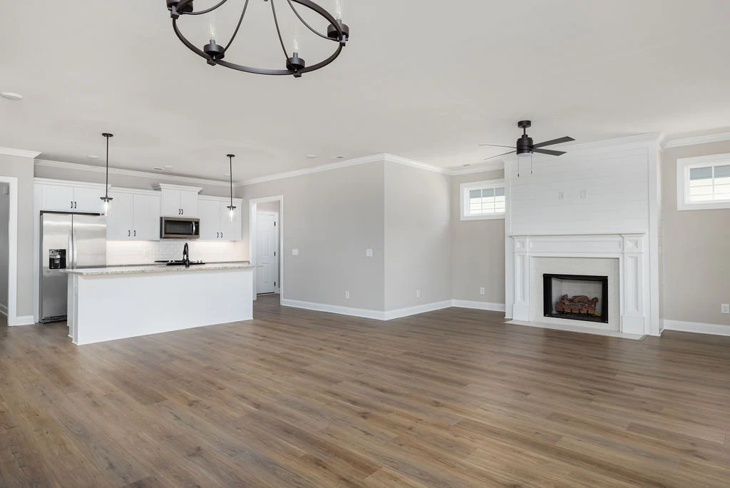 Spacious open-concept kitchen and living area with hardwood floors, white cabinets, stainless appliances, and a fireplace. Built by Pratt Home Builder