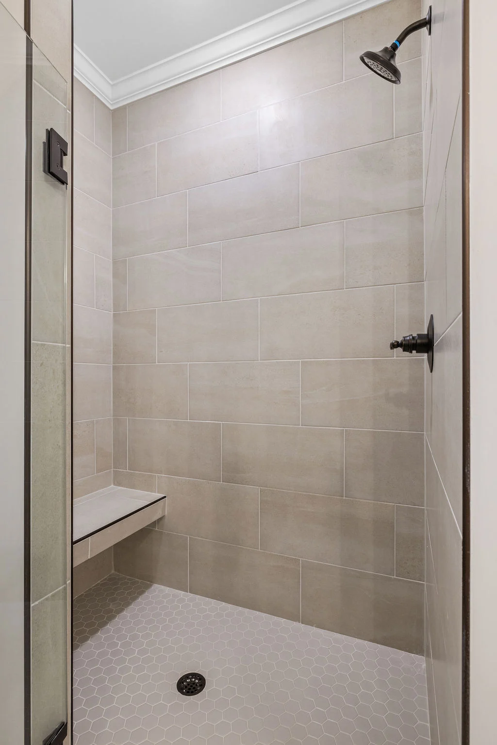Modern shower with beige tiles, rainfall showerhead, and built-in bench. Designed by Pratt Home Builders in Chattanooga TN.